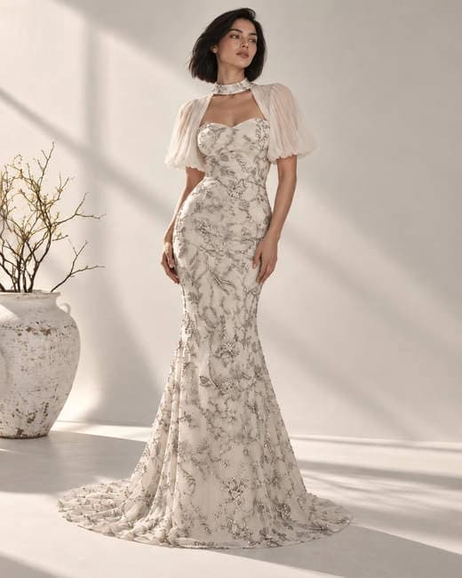 Model wearing an embroidered ivory gown in a sunlit room